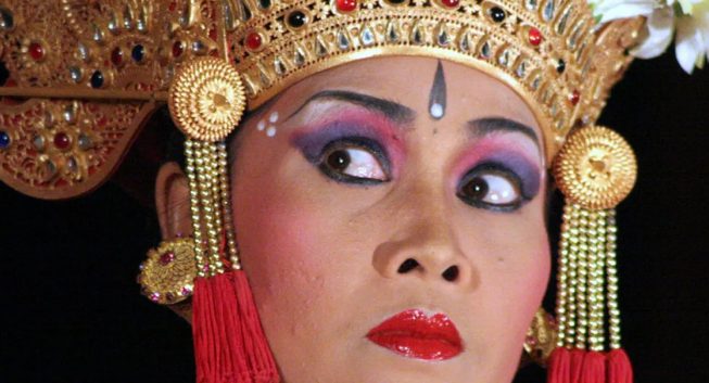 A performer wearing a gold headdress, bright makeup, and a dramatic expression.