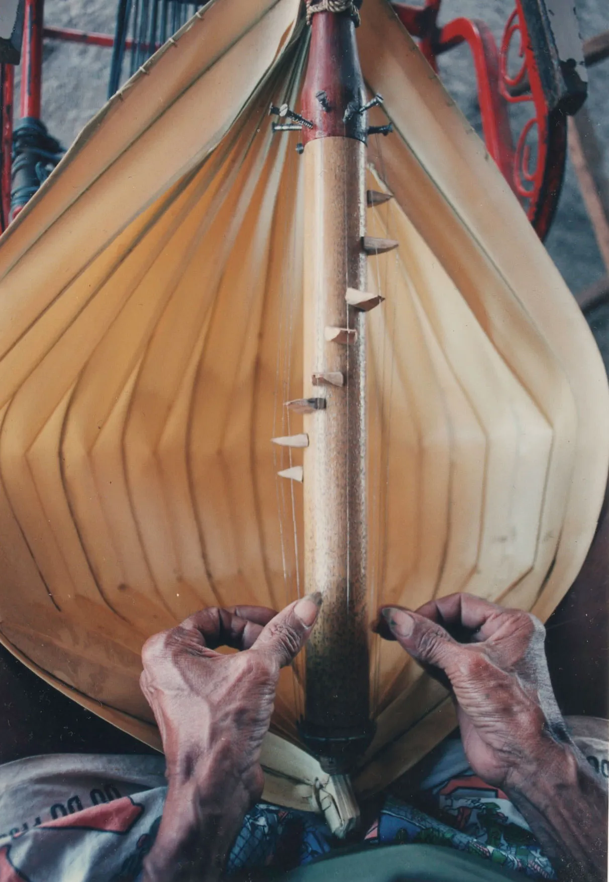 Weathered fingers pluck at the strings of a sasandu, from the player's perspective.