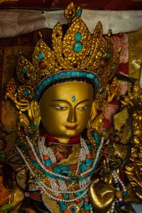 Figure 3. Close up of a crowned golden goddess sculpture draped with pearls and jewels in front of a brocade fabric backdrop.