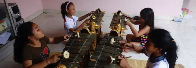 Four children sitting on the floor playing gamelan