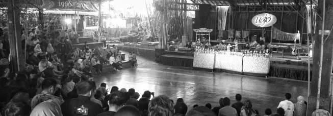 Black and white photo of a crowd watching a gamelan performance in a large performance space