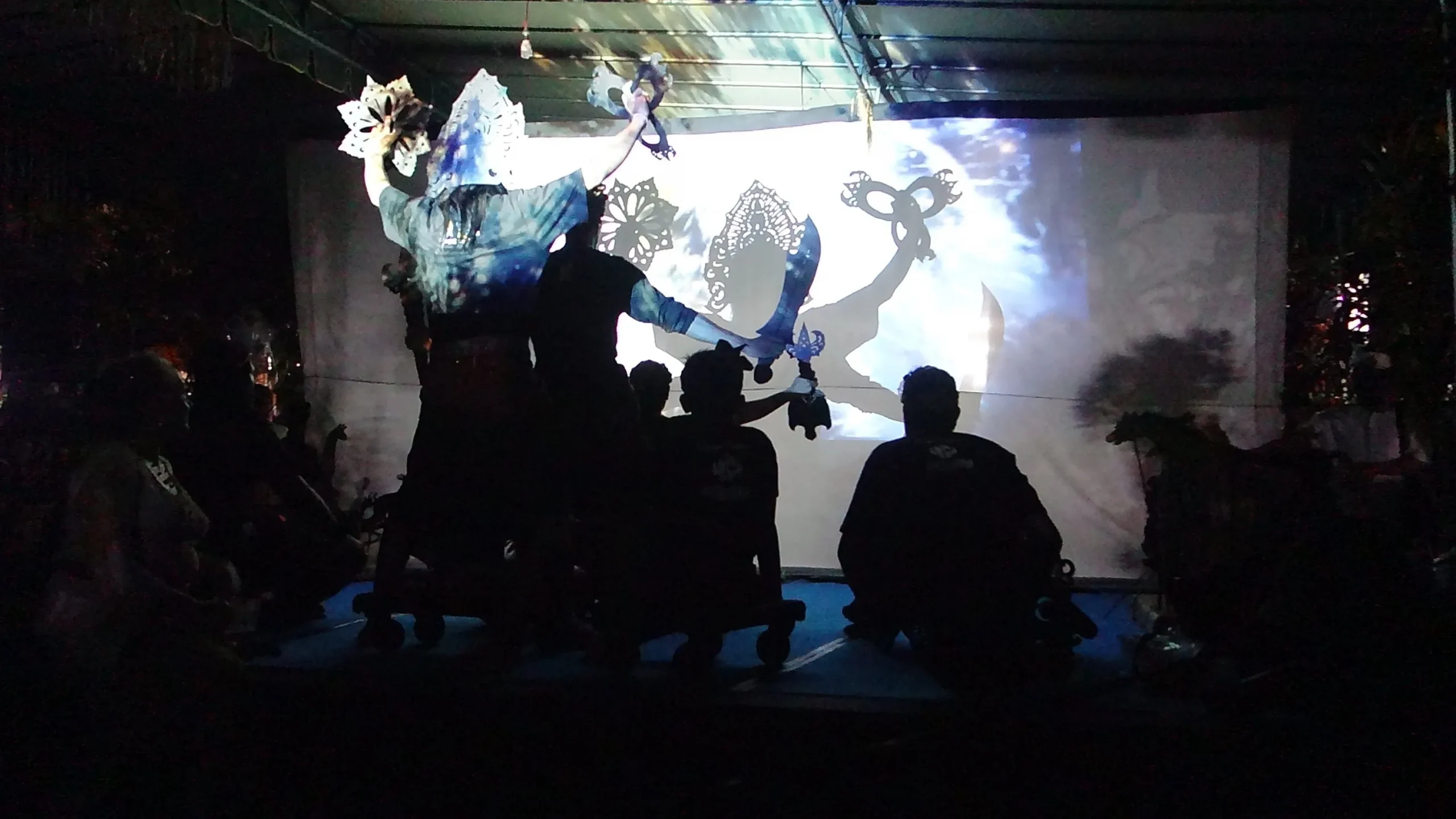 Puppeteers and dancers casting silhouettes onto the backside of a screen.