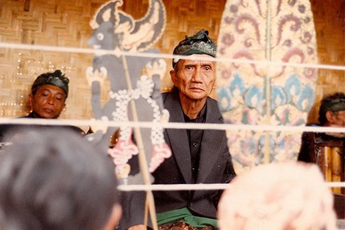 Wayang performer looking out between two paper puppetry figures.