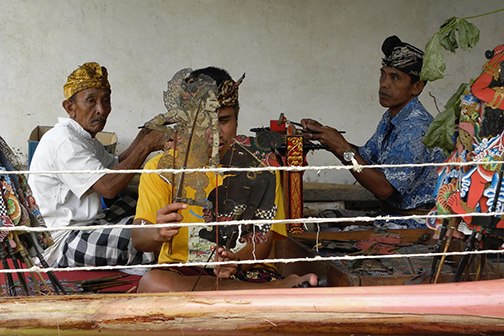 a man practicing wayang lemah puppetry with two gender wayang players in the background.