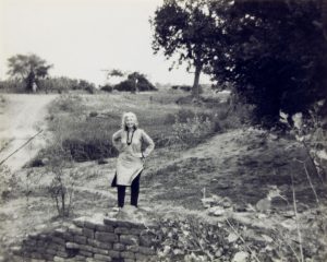 photograph of a woman standing next a stone wall by the roadside