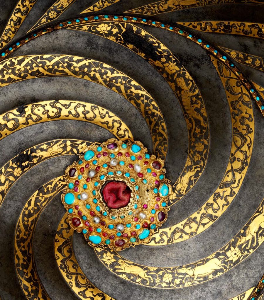 Tsars and the East book cover. Cover image: Dark gray metal covered with a cold swirling pattern that meets at a bejeweled center point. The gold swirls are filled with animal and floral designs. The center of the swirl features a red stone surrounded by turquoise and burgundy stones and white pearls