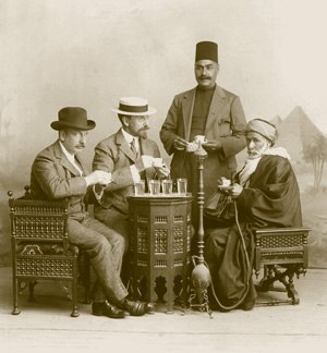 Charles Lang Freer at a table with three other men, with some glasses of clear liquid on the table and a hookah amidst them, a pyramid backdrop behind them.