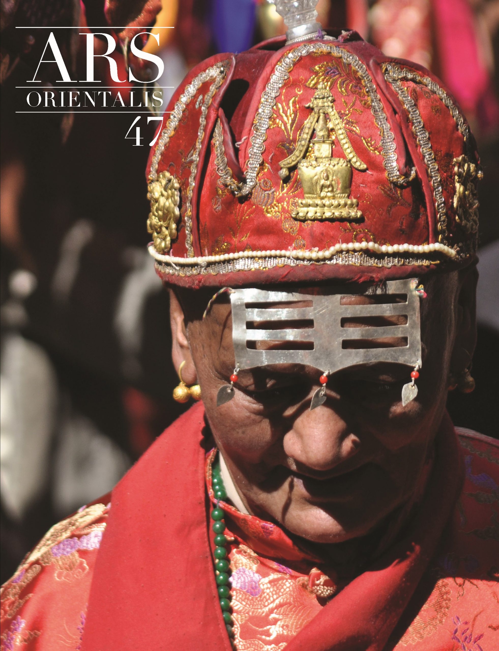 Ars Orientalis, volume 47 book cover. Cover image: Close up of a person's face looking down, half their face cast in shadow. On their head is an ornate red cap decorated with gold ornaments, pearl lining, and silver embroidery.