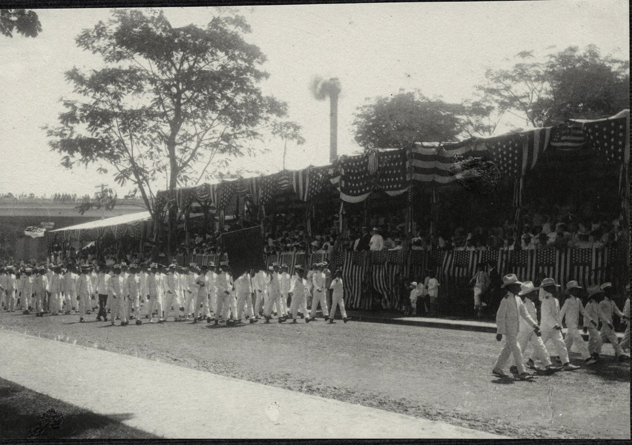 Manila: Group of American soldiers with banner march before viewing stand