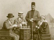 Charles Lang Freer at a table with three other men, with some glasses of clear liquid on the table and a hookah amidst them, a pyramid backdrop behind them.