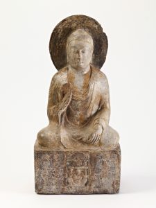 a small limestone buddha, seated, with one hand raised