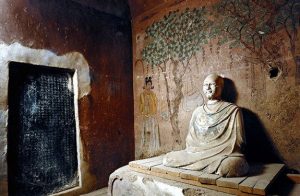 A buddha sculpture seated in a room with a panting behind