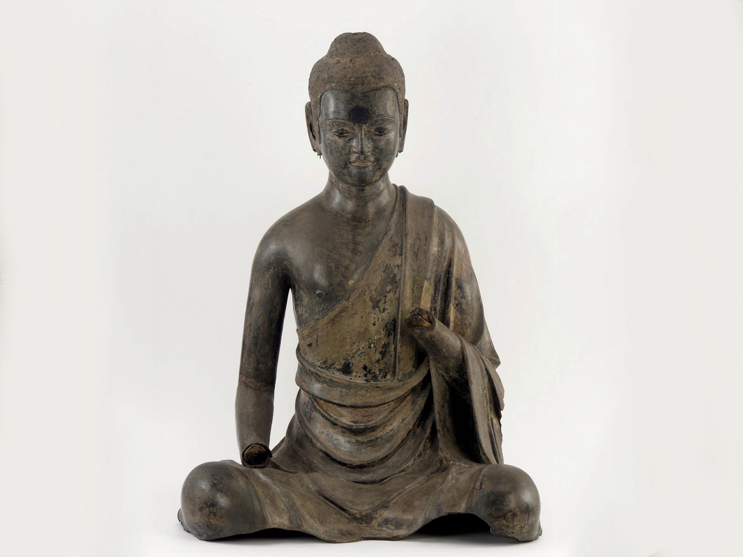 Dry lacquer figure depicting the Sakyamuni Buddha sitting dressed in a robe with hands missing and long earlobes broken off.