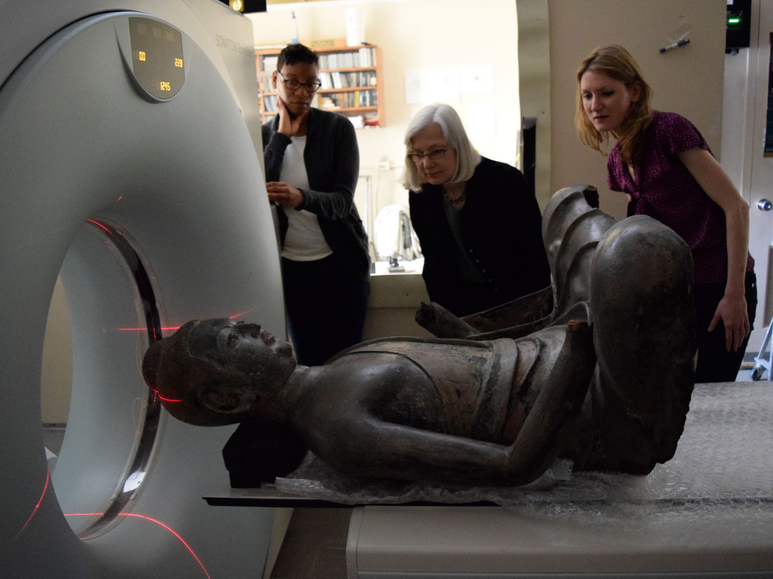 Conservators observe the Freer Buddha statue entering an instrument for CT scanning.