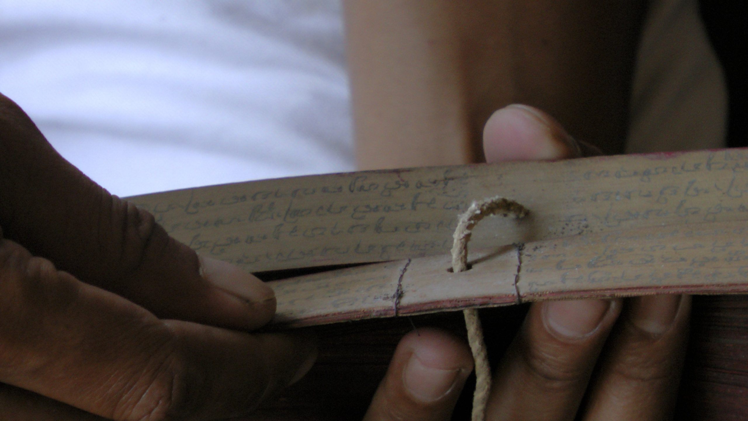 Hands holding two leaves of a lontar manuscript, bound with rough string.