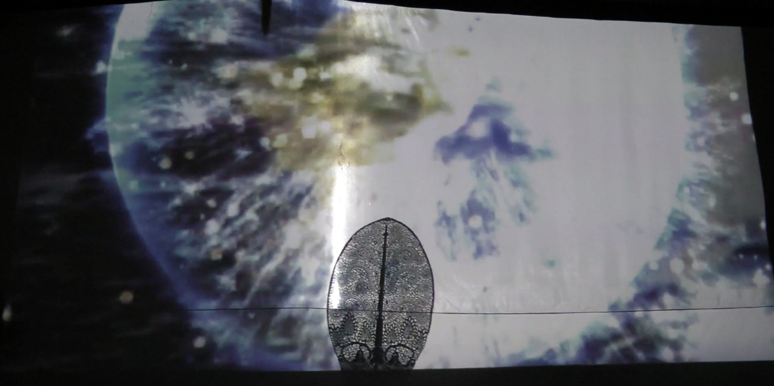 The shadow of an ornate kayon puppet, in front of a background that appears to be a shimmering, glowing globe.