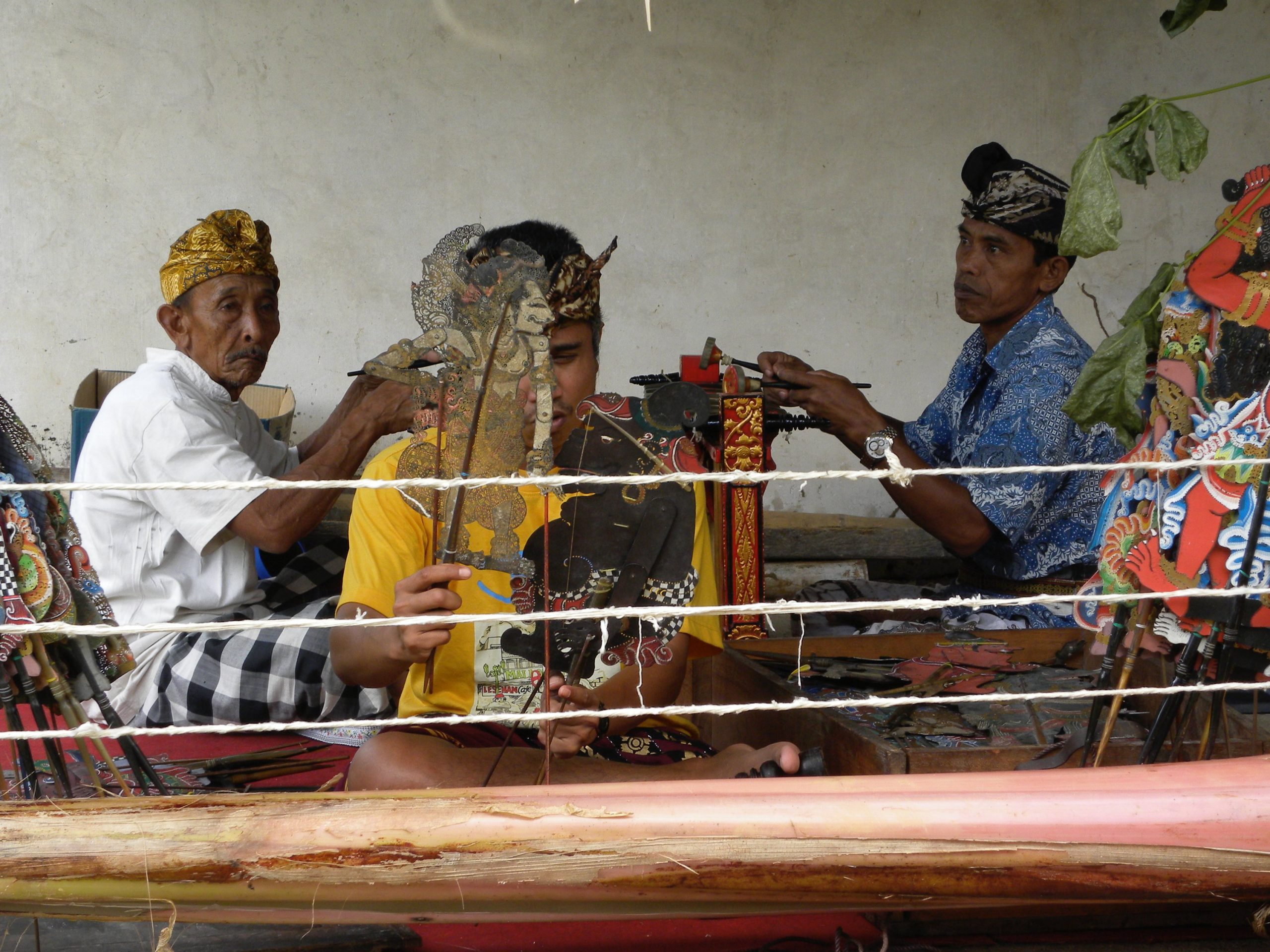 A man practicing wayang lemah puppetry with two gender wayang players in the background.