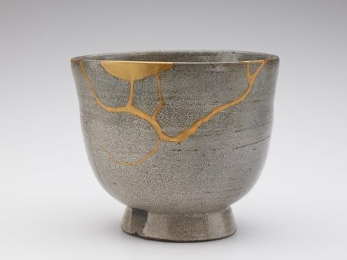 A white-gray, stone tea bowl with a crackled surface. A crack along the bowl is filled in with gold