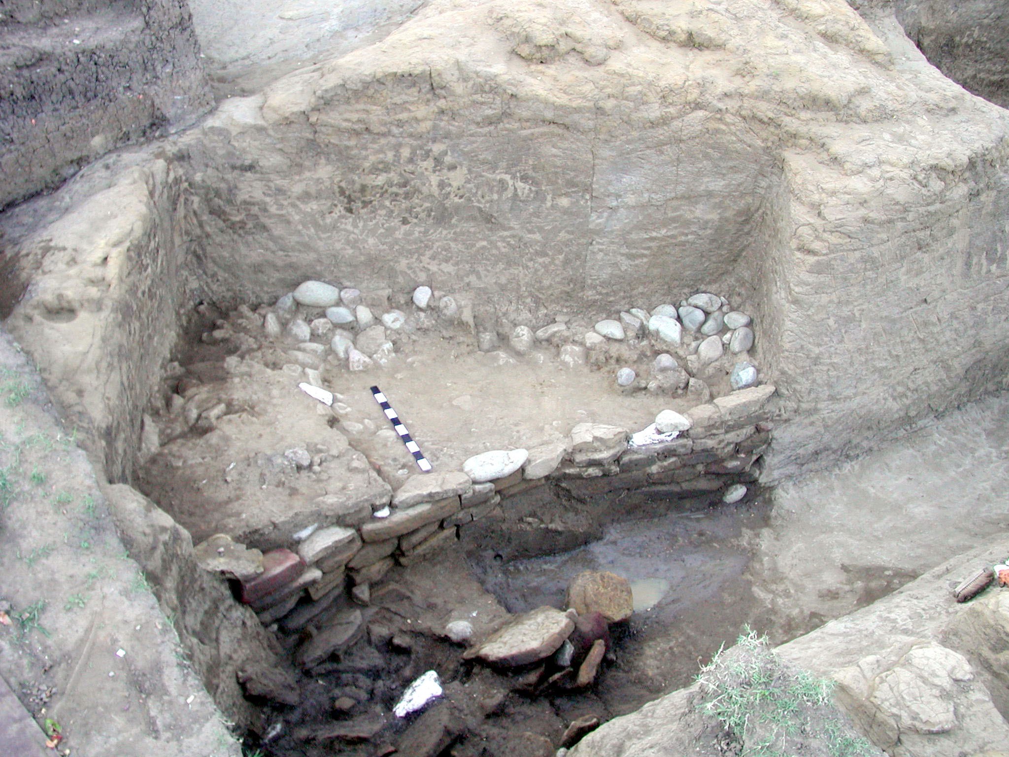 Vani excavation site: Grave 24. In the photograph you can see Grave 24 and just in front, the channel, with part of the channel wall visible just in front of the tomb.