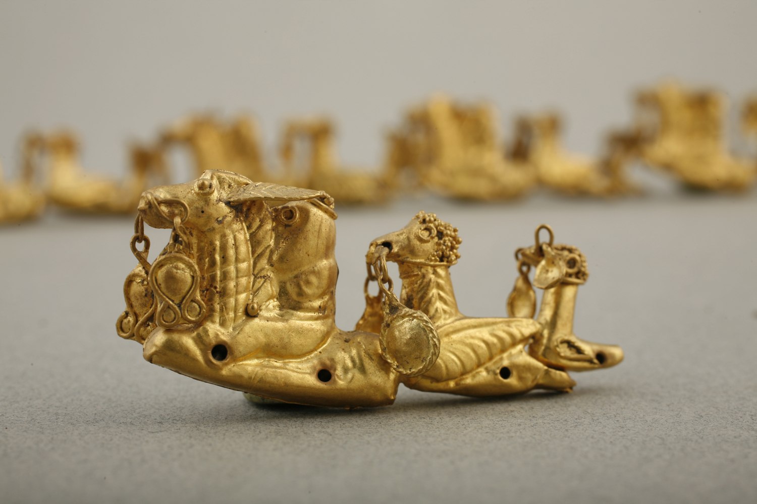 elaborate headdress, the most prominent are the fourteen groups of highly stylized riders accompanied by two birds. The birds each have disks suspended from their beaks, and they were sewn to a supporting fabric by means of the holes along the bottom.