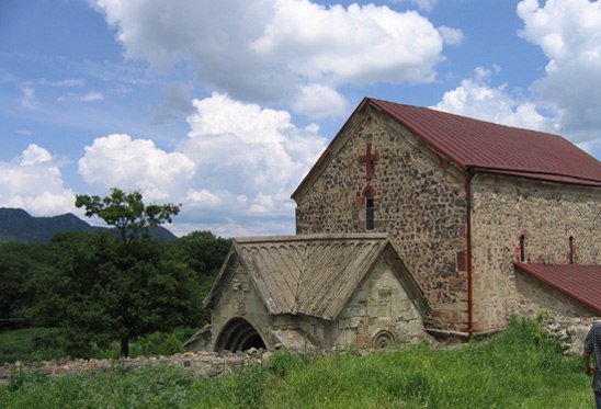 View of the Dmanisi Sioni basilica, 2 stone buildings, one with a red roof and the other with a tan roof.