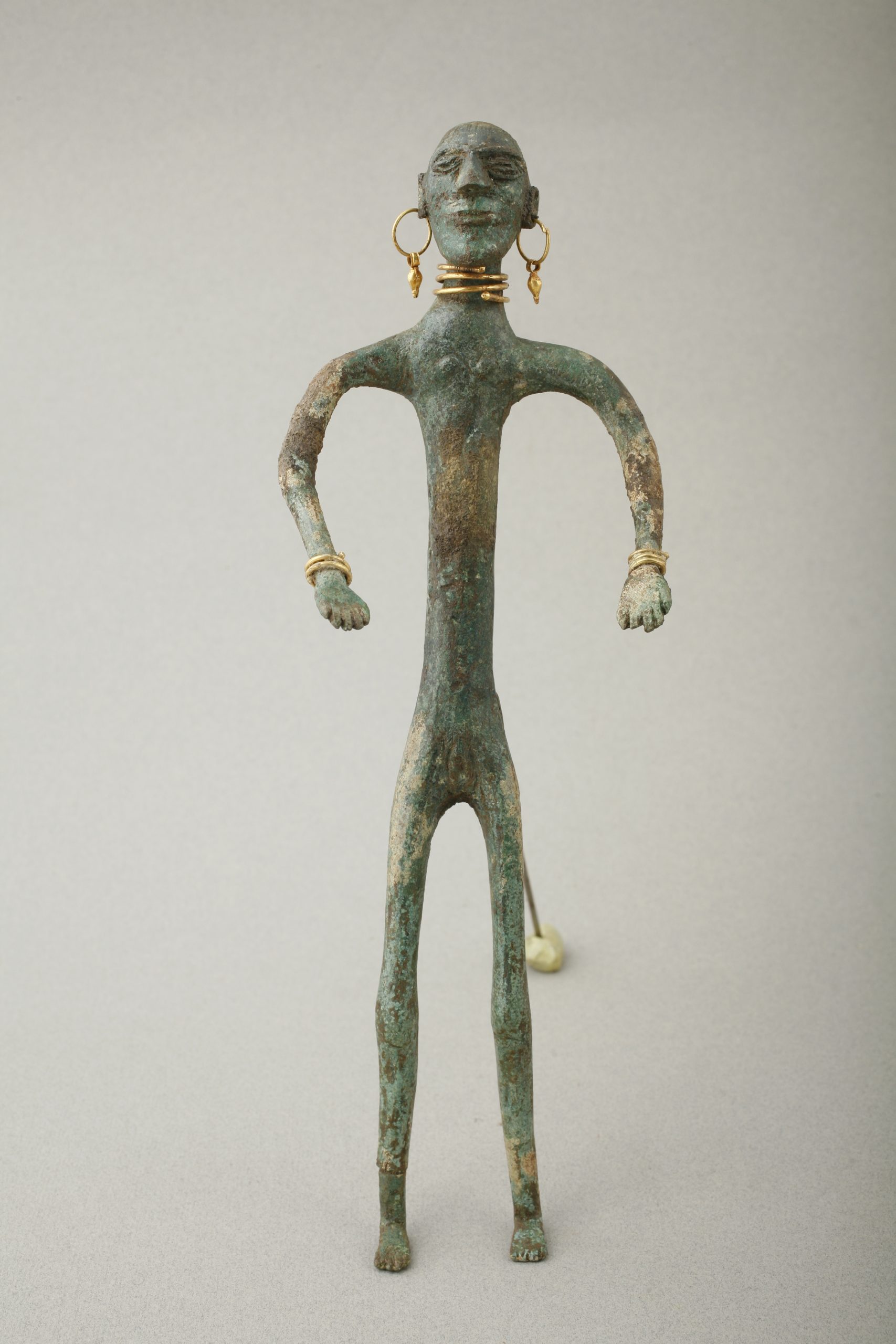 stylized statuette figure of a man wearing gold jewelry—a torque, bangles, and earrings.