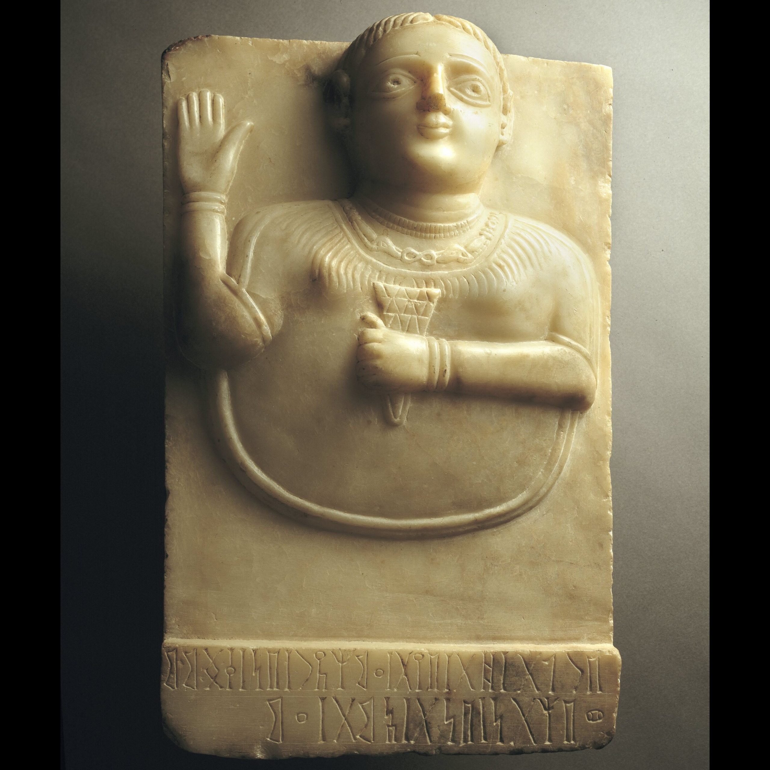 Alabaster stela depicting female holding a sheaf of wheat