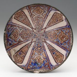 Overhead view shows a round bowl with a geometric design radiating from the center in red, gold, blue, and green on white glaze.
