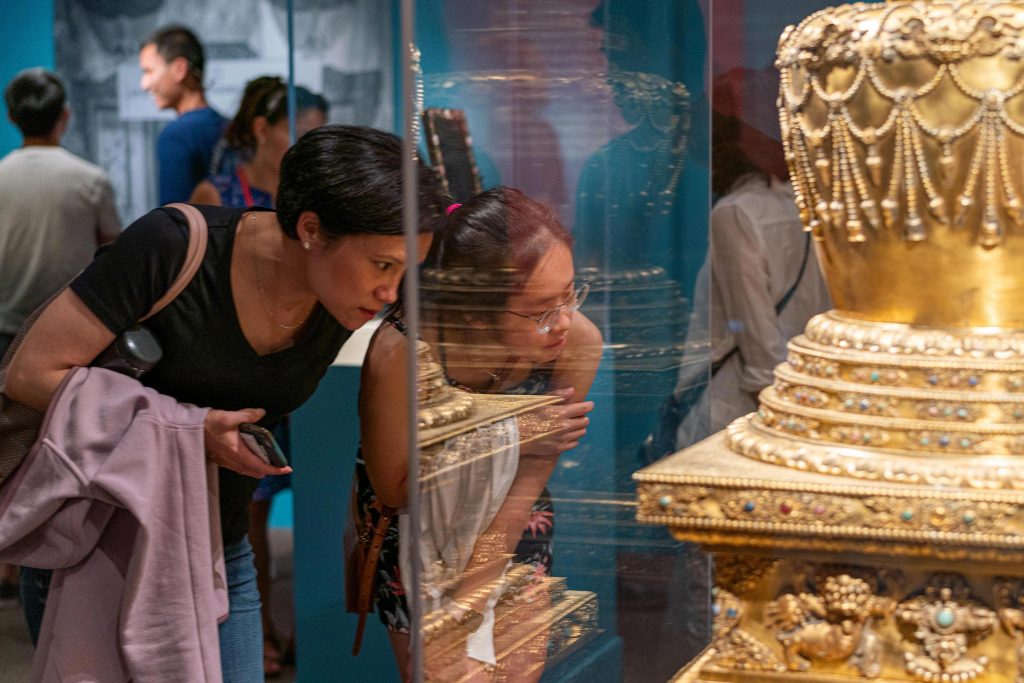 Two museum visitors bend over to look closely at an object in a display case.