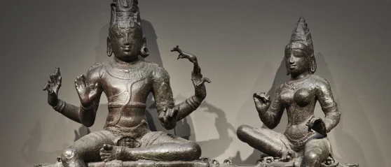 view of two sculptures, both seated, one with four arms and hands in different gestures, the other, smaller, with two hands also making gestures.