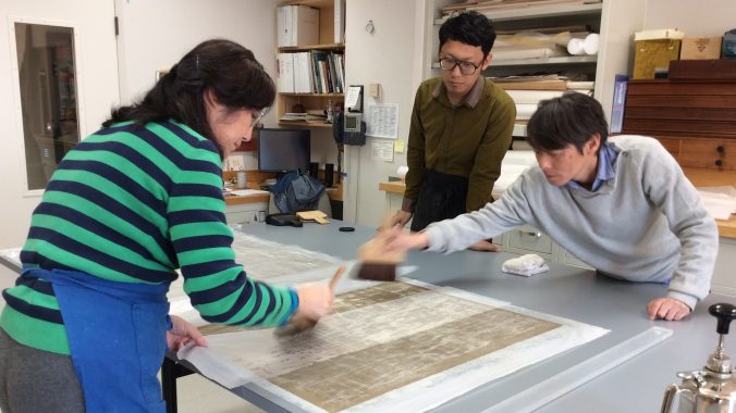 three conservators holding brushes and working on paper work
