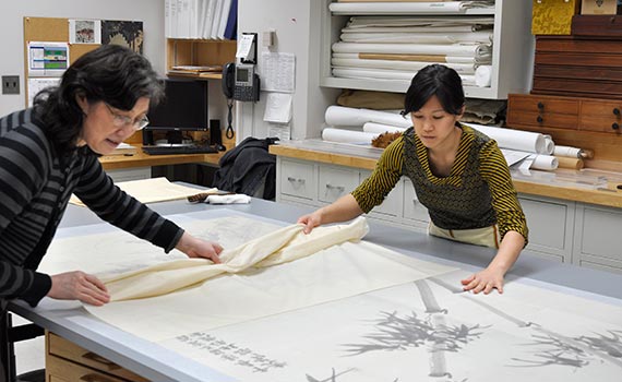photo of 2 conservators rolling up a canvas