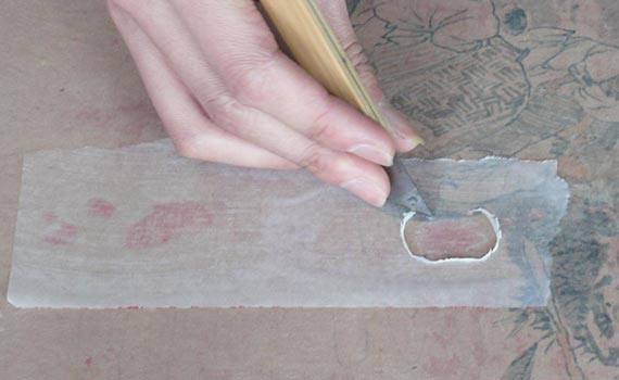 photo of a hand holding a mat knife cutting a piece of fabric