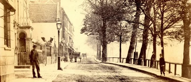 Sepiatone photo of an old London street, with a man standing near a streetlight on one side and a row of trees on the other.