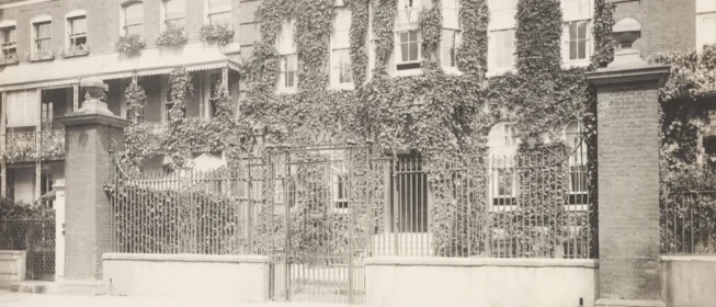 Black and white photo of the front gate of an ivy-covered home.