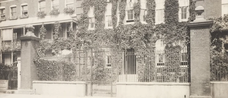 Black and white photo of the front gate of an ivy-covered home.
