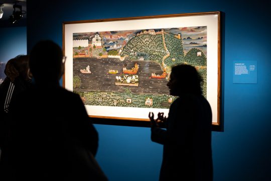 Curator and guests silhouetted against a detailed painting during a tour.